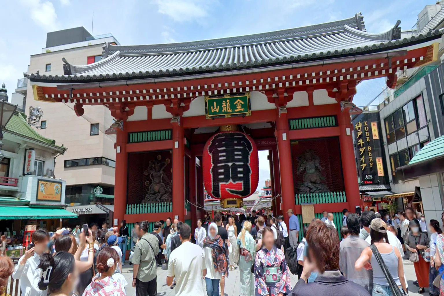 A massive red lantern hanging at the entrance of Kaminarimon Gate in Asakusa, Tokyo, with crowds of visitors walking beneath it in a lively downtown atmosphere.