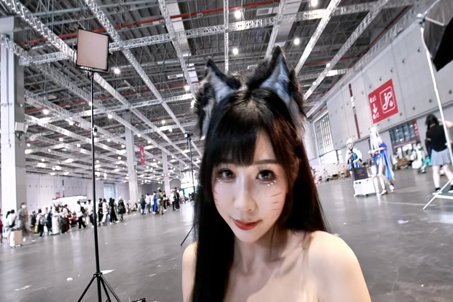 アニメイベント会場での実写映像。猫耳コスチュームを着たキャラクターが、会場の中央でインタラクティブなポーズを決めているよ。