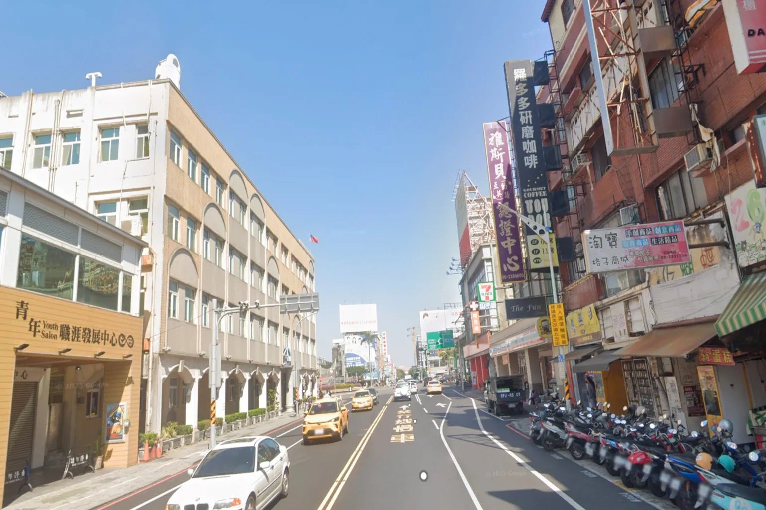 台南の市街地が続く風景。青空の下、大通りを車がゆったり走り、通り沿いには地元の店やバイクが並ぶ。