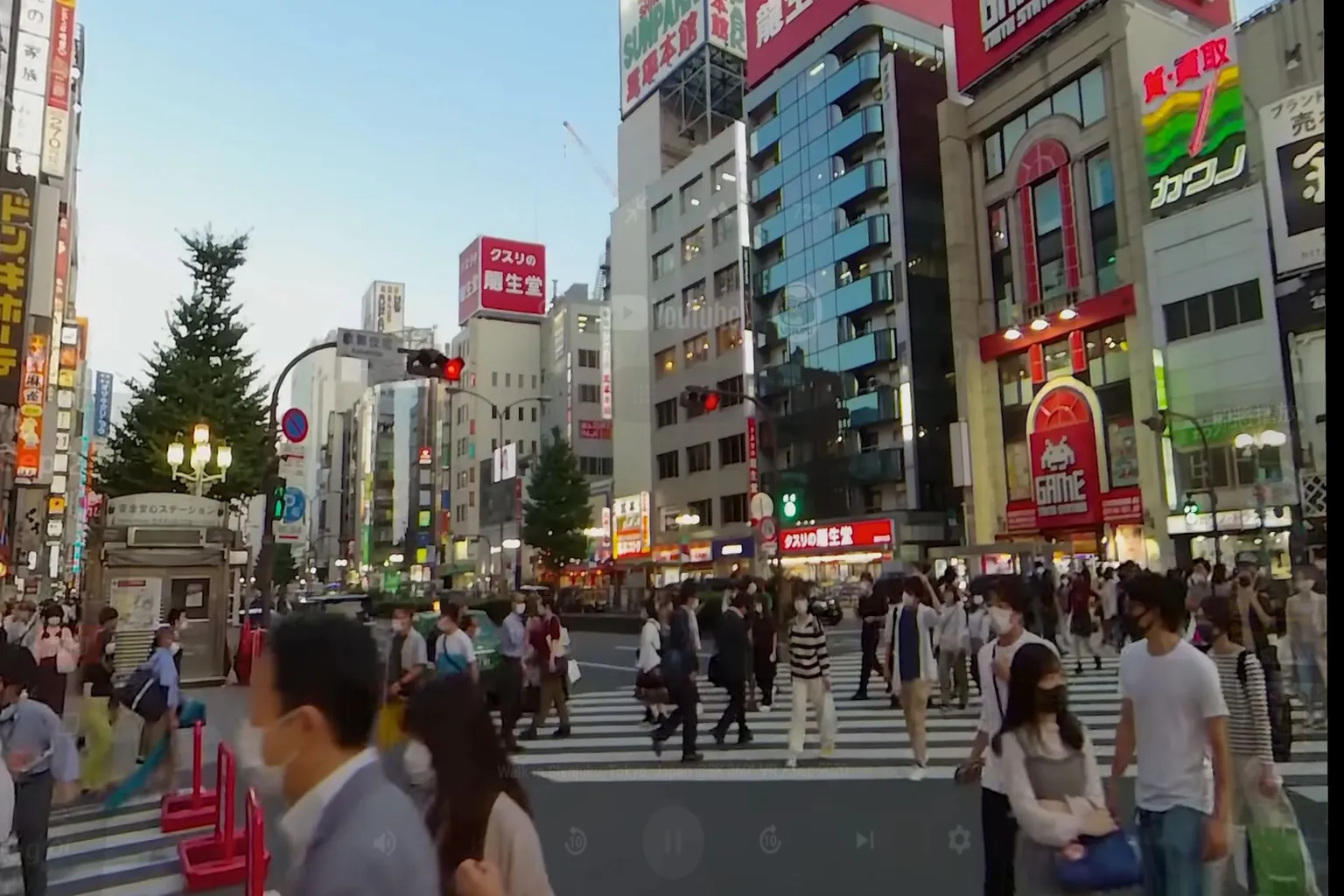 日本・新宿の交差点。夕暮れ時の街に人波とネオンがあふれ、VRならではの没入感ある都会の雰囲気。